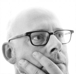 bald male with glasses with his hand on his face thinking